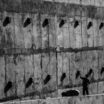 Dois trabalhadores pintam uma grande parede de concreto em um ambiente de trabalho.