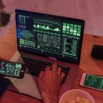 Pessoa trabalhando com software de cibersegurança em um notebook e usando um smartphone.