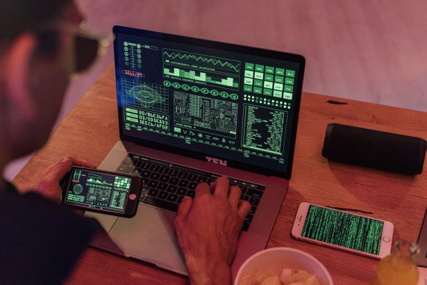 Pessoa trabalhando com software de cibersegurança em um notebook e usando um smartphone.