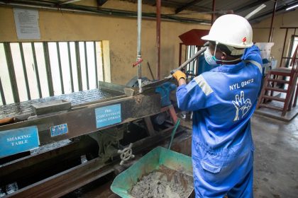 Trabalhador usando uniforme azul opera uma mesa vibratória para processamento de minério em uma unidade industrial.