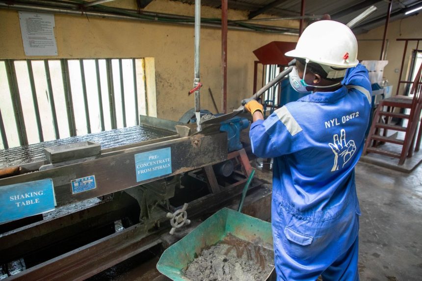 Trabalhador usando uniforme azul opera uma mesa vibratória para processamento de minério em uma unidade industrial.