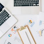 Vista superior de laptops, gráficos e relatórios usados para análise de dados financeiros sobre uma mesa.