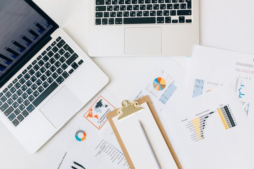 Vista superior de laptops, gráficos e relatórios usados para análise de dados financeiros sobre uma mesa.
