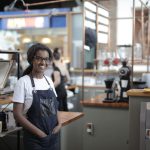 Empreendedor sorrindo atrás do balcão de um café, em seu local de trabalho