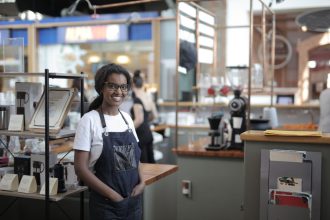 Empreendedor sorrindo atrás do balcão de um café, em seu local de trabalho