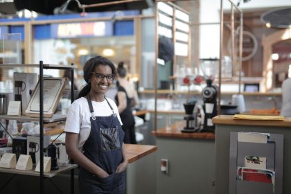 Empreendedor sorrindo atrás do balcão de um café, em seu local de trabalho