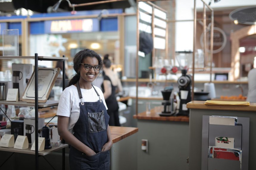 Empreendedor sorrindo atrás do balcão de um café, em seu local de trabalho